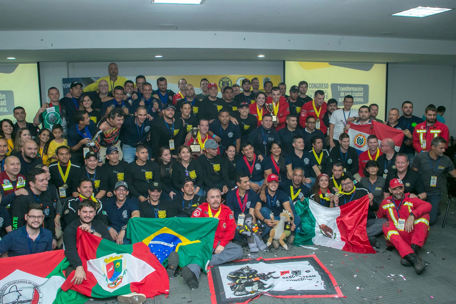 Fotografía grupal de rescatistas de distintos países con banderas latinoamericanas