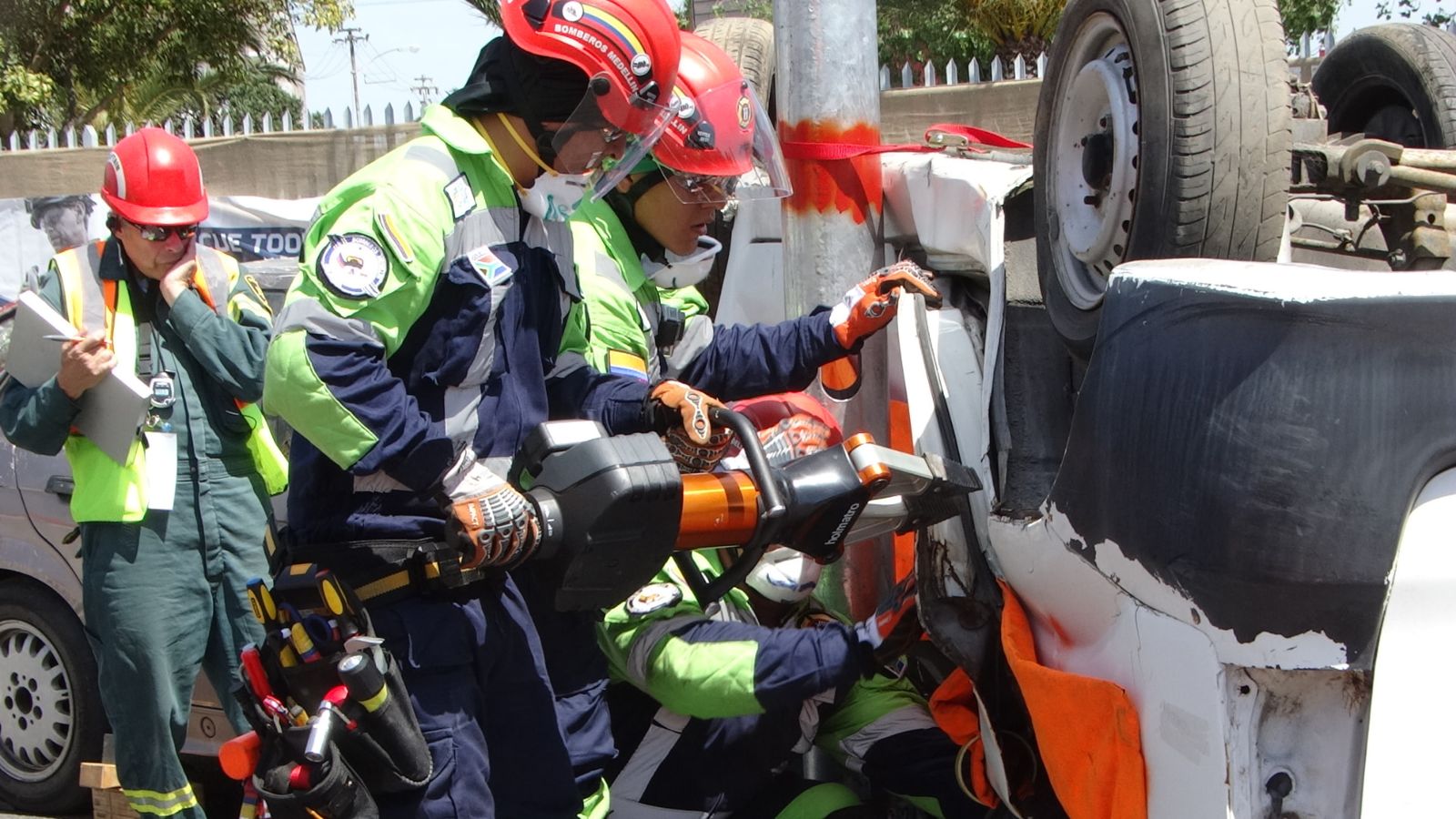 Rescatistas con casco operan una herramienta hidráulica junto a un vehículo volcado durante un entrenamiento